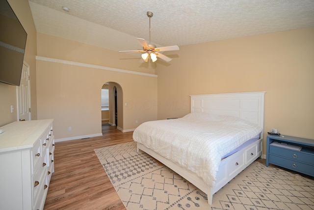 bedroom with baseboards, a textured ceiling, a ceiling fan, arched walkways, and light wood finished floors