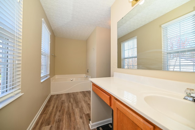 full bathroom featuring baseboards, a textured ceiling, vanity, wood finished floors, and a garden tub