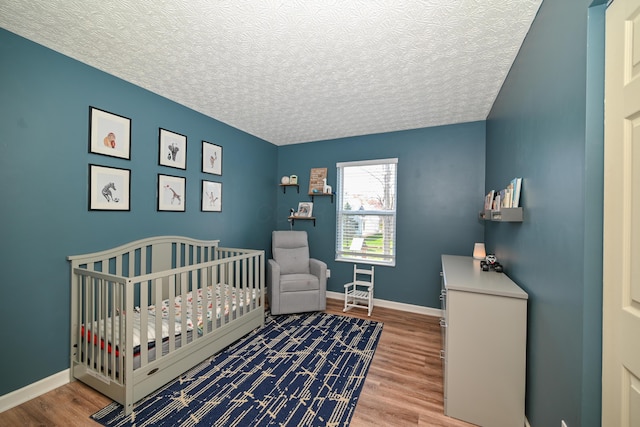 bedroom featuring baseboards, a crib, and wood finished floors