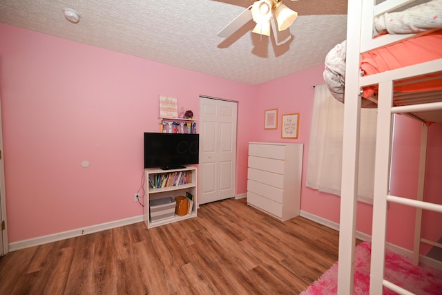 unfurnished bedroom featuring a textured ceiling, baseboards, a ceiling fan, and wood finished floors