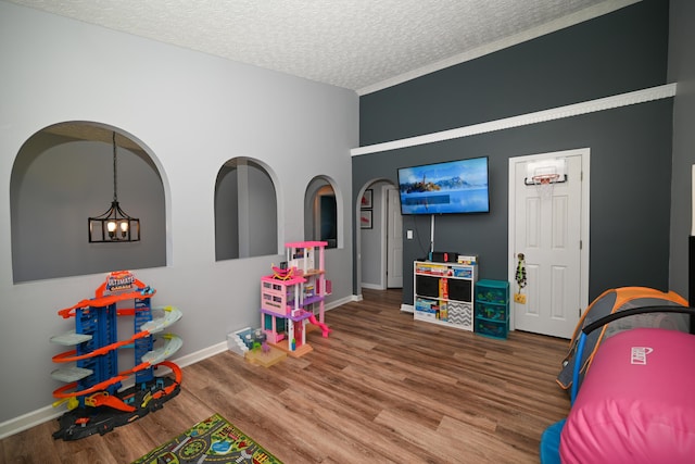 playroom featuring a textured ceiling, wood finished floors, baseboards, and a notable chandelier