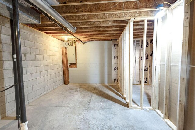 unfinished basement featuring concrete block wall and electric panel