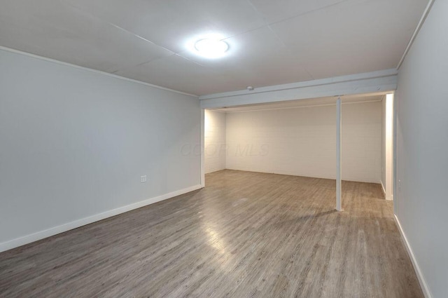 interior space featuring baseboards, crown molding, wood finished floors, and concrete block wall