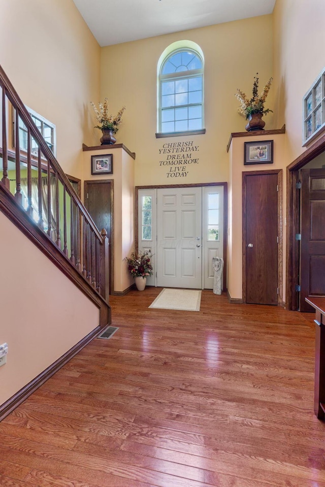 foyer entrance featuring wood finished floors, a high ceiling, stairs, and visible vents