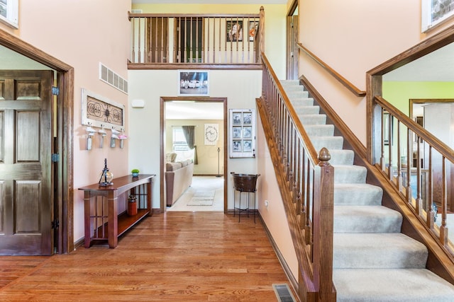 stairs featuring a towering ceiling, wood finished floors, visible vents, and baseboards