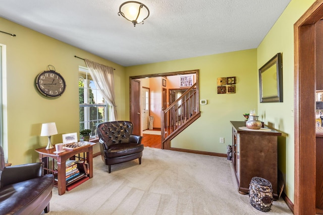 sitting room with baseboards, carpet flooring, a textured ceiling, and stairs