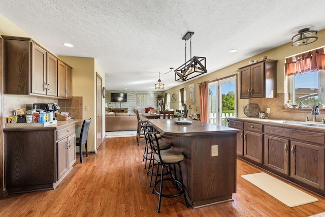 kitchen with wood finished floors, a sink, decorative backsplash, a kitchen bar, and a kitchen island