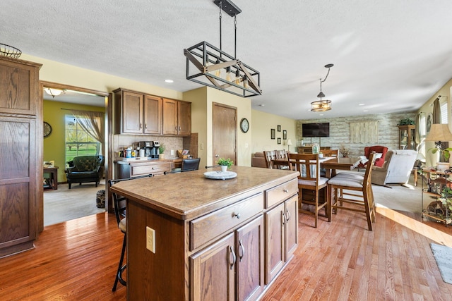 kitchen with light wood-type flooring, a center island, hanging light fixtures, a textured ceiling, and open floor plan