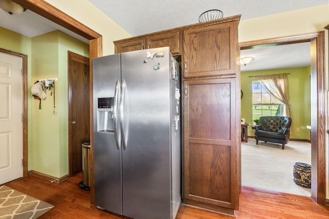 kitchen featuring wood finished floors, stainless steel refrigerator with ice dispenser, and baseboards