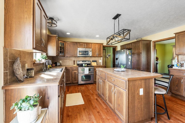 kitchen with a sink, dark wood finished floors, light countertops, a kitchen island, and appliances with stainless steel finishes