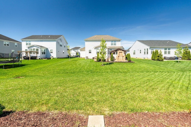 rear view of house with a residential view, a trampoline, and a yard