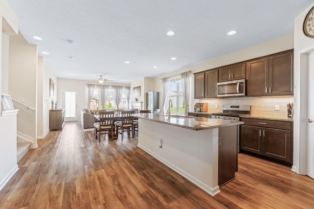 kitchen with dark wood-style flooring, a center island with sink, light stone counters, a sink, and stainless steel appliances