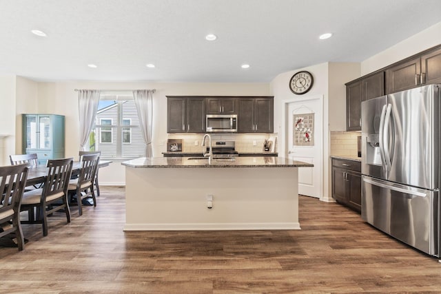 kitchen with dark wood-style flooring, dark brown cabinetry, appliances with stainless steel finishes, and dark stone countertops