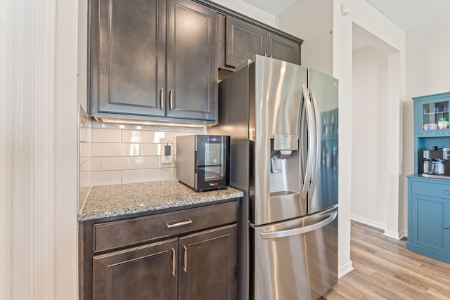 kitchen with dark brown cabinets, light wood-style flooring, baseboards, decorative backsplash, and stainless steel refrigerator with ice dispenser