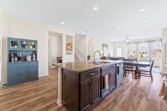 kitchen featuring ceiling fan, a sink, light wood finished floors, dark stone counters, and stainless steel dishwasher