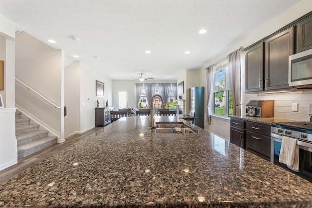 kitchen featuring dark brown cabinetry, appliances with stainless steel finishes, a sink, recessed lighting, and a large island