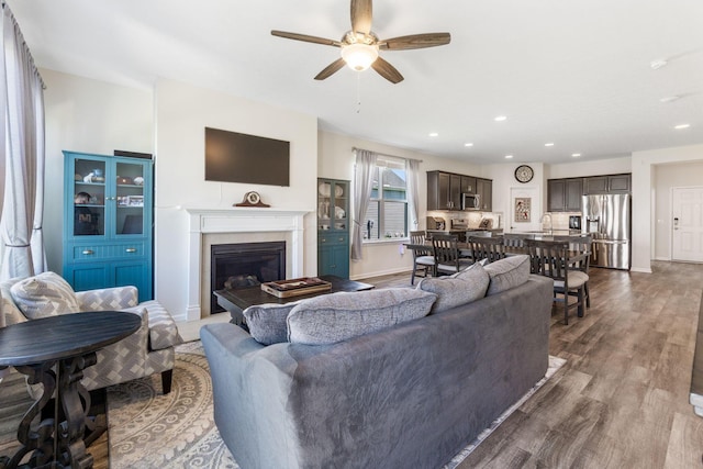 living area featuring ceiling fan, a glass covered fireplace, recessed lighting, baseboards, and dark wood-style floors