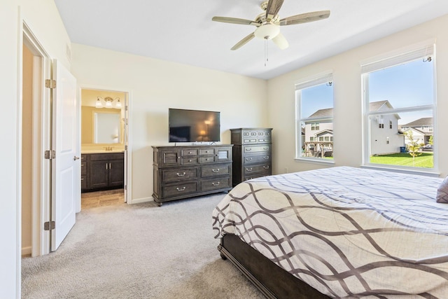 bedroom with baseboards, ensuite bathroom, light carpet, and ceiling fan