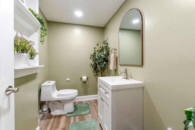 bathroom with wood finished floors, vanity, baseboards, toilet, and recessed lighting