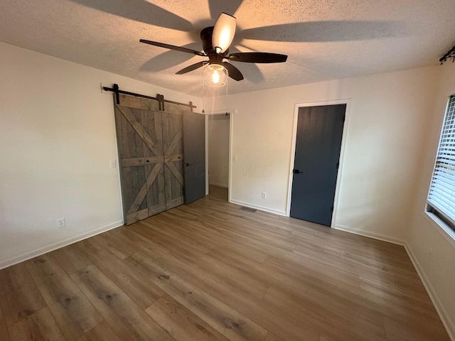 7326 State Route 19 Unit 2, Lot 321, Mount Gilead, OH 43338 - unfurnished bedroom featuring a textured ceiling, a barn door, wood finished floors, baseboards, and ceiling fan