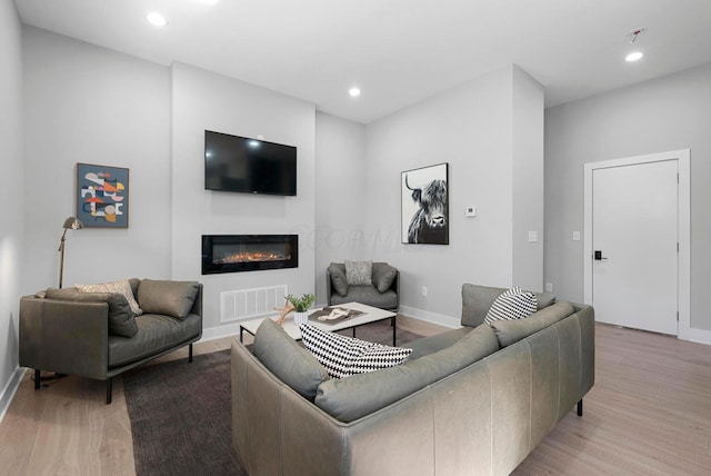 living room with a glass covered fireplace, light wood-type flooring, baseboards, visible vents, and recessed lighting