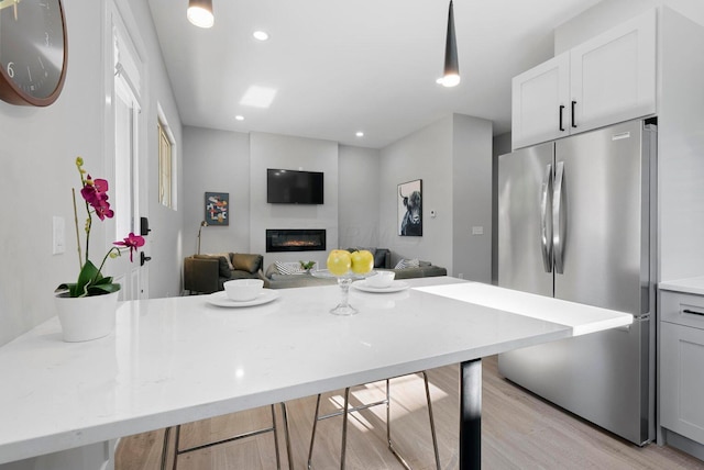 kitchen with light stone counters, freestanding refrigerator, a kitchen breakfast bar, a glass covered fireplace, and open floor plan
