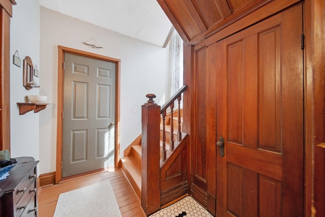 foyer entrance featuring baseboards, light wood-style floors, and stairway