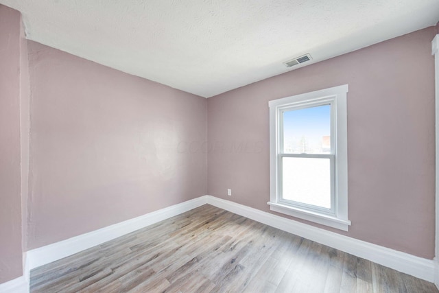 spare room with baseboards, a textured ceiling, visible vents, and light wood-style floors