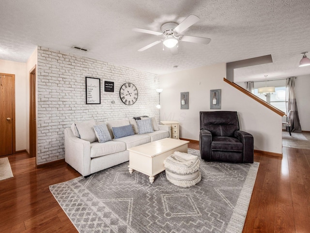 living room featuring visible vents, wood finished floors, brick wall, and a ceiling fan