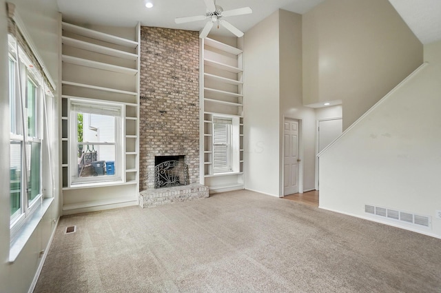 unfurnished living room with carpet, built in shelves, a ceiling fan, high vaulted ceiling, and a brick fireplace
