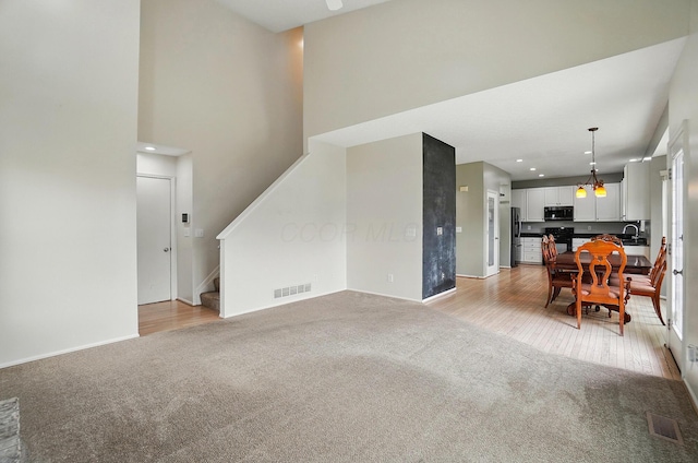 living room featuring light carpet, stairs, a high ceiling, baseboards, and a chandelier