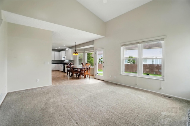 living room featuring light carpet, baseboards, high vaulted ceiling, and a chandelier