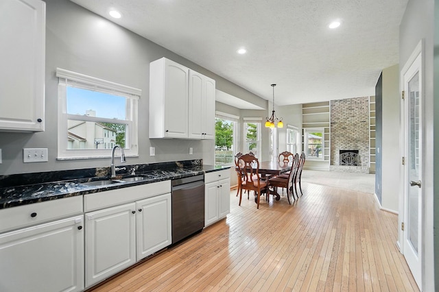kitchen with dishwasher, a sink, white cabinetry, light wood-style floors, and dark stone counters