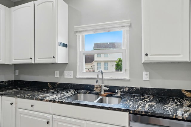 kitchen featuring stainless steel dishwasher, a sink, white cabinetry, and dark stone counters