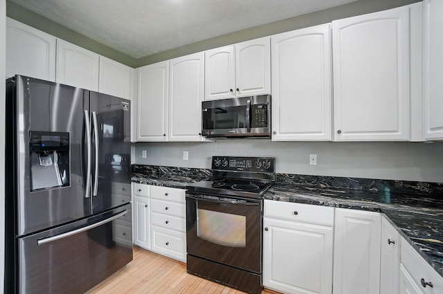 kitchen featuring appliances with stainless steel finishes, white cabinetry, light wood finished floors, and dark stone countertops