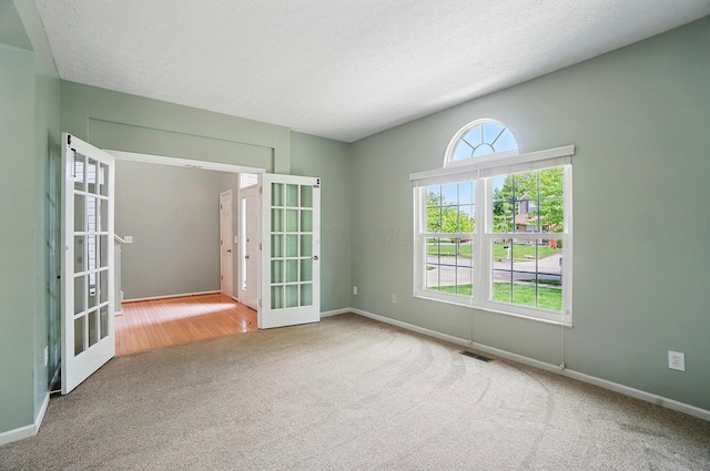 carpeted empty room with french doors, a textured ceiling, and baseboards