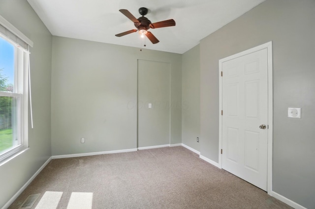 carpeted spare room with healthy amount of natural light, a ceiling fan, and baseboards