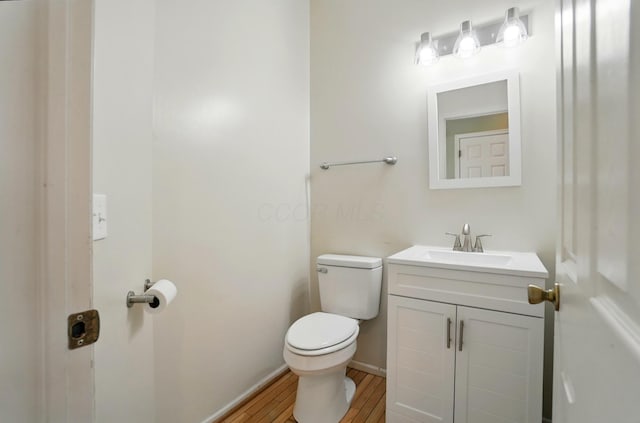 half bathroom featuring toilet, vanity, wood finished floors, and baseboards