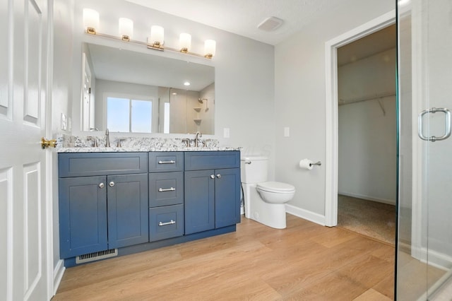 bathroom with a shower stall, wood finished floors, toilet, baseboards, and double vanity