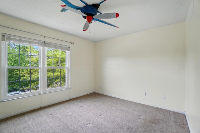 carpeted spare room featuring ceiling fan and baseboards