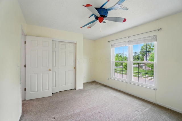 unfurnished bedroom with carpet flooring, baseboards, a closet, and a ceiling fan