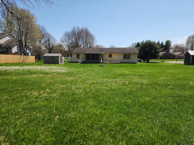 rear view of house featuring a yard, a storage shed, an outdoor structure, and fence