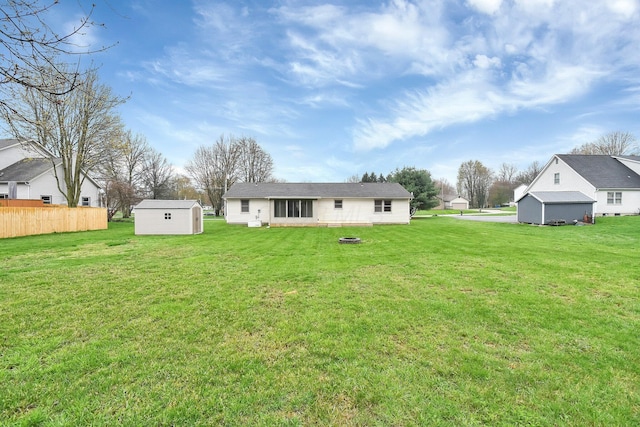 back of property with a shed, an outdoor structure, fence, and a lawn