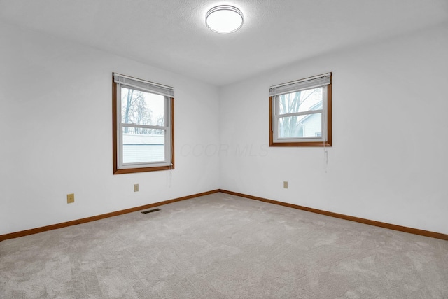 carpeted spare room featuring plenty of natural light, visible vents, and baseboards