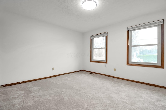 carpeted empty room featuring a textured ceiling, baseboards, and visible vents