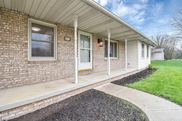 entrance to property featuring a porch, a yard, and brick siding