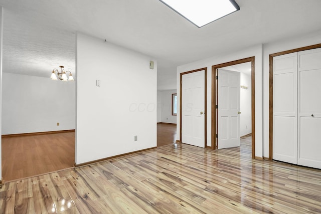 unfurnished bedroom featuring baseboards, light wood-type flooring, and an inviting chandelier