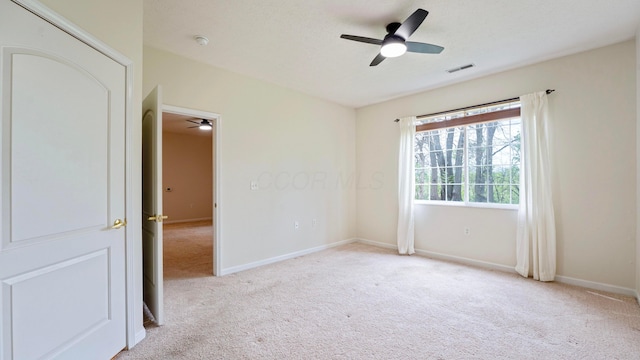 spare room featuring visible vents, ceiling fan, and light carpet