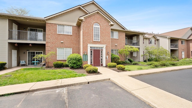 view of front of property with uncovered parking, a front lawn, a balcony, and brick siding