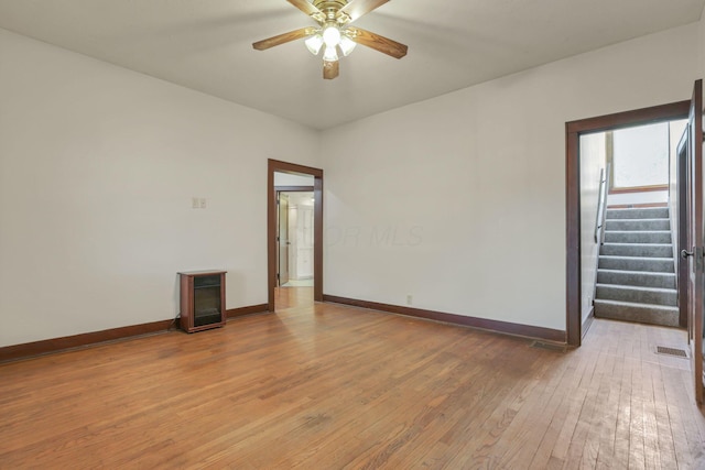 spare room with stairs, light wood-style floors, ceiling fan, and baseboards